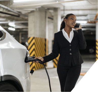 A woman connects a charging cable to an electric car, preparing to recharge its battery at a charging station