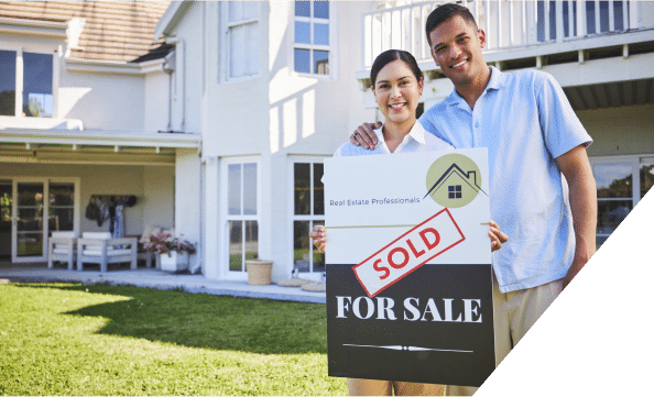 A happy couple stands in front of their newly purchased house, smiling and holding a "Sold" sign