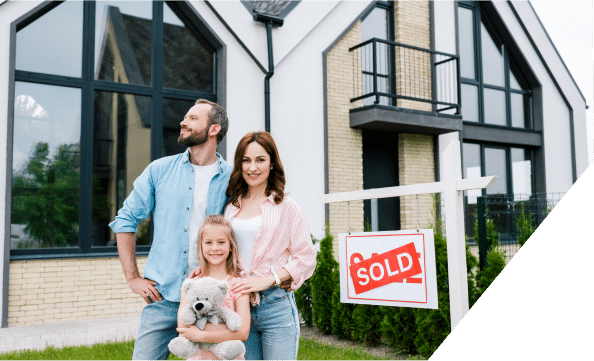 A happy family poses in front of their new house, proudly displaying a sold sign to mark their successful home purchase