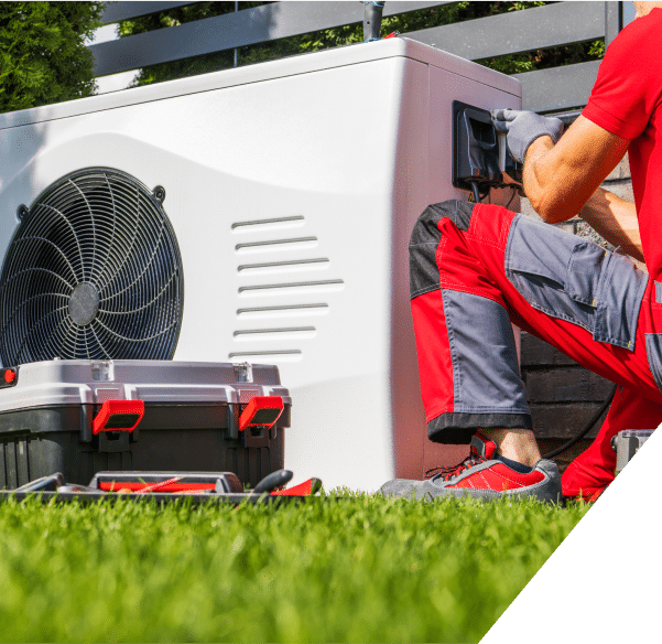 A man in a red shirt is repairing an air conditioning unit, focused on his task with tools in hand